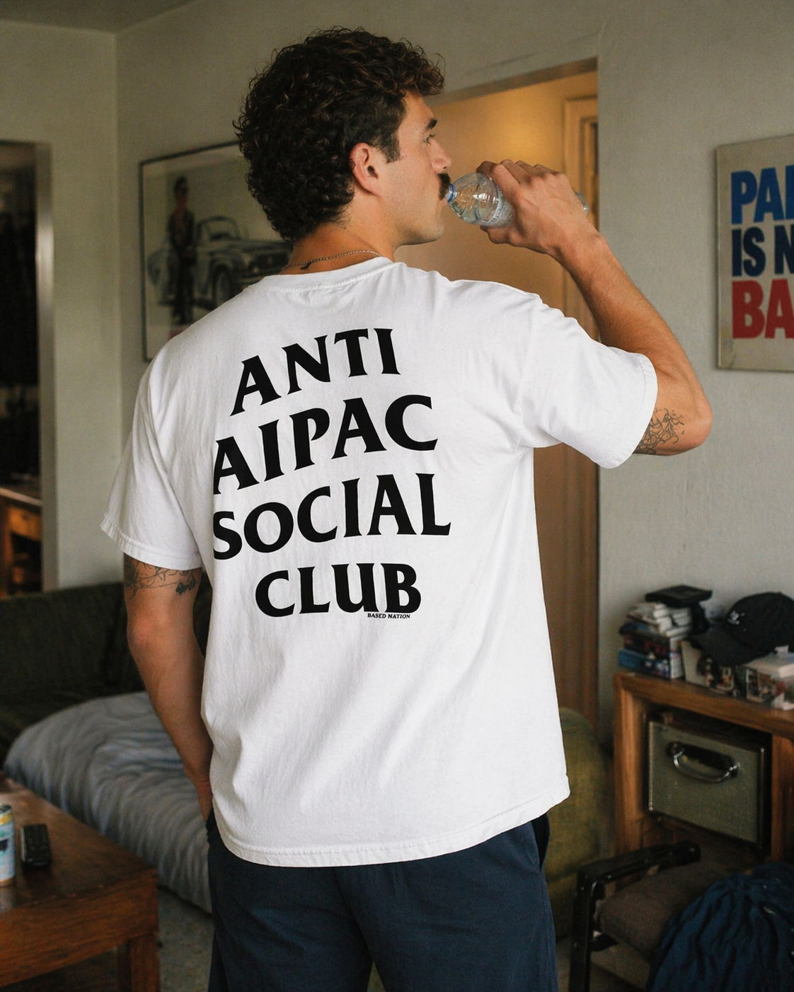 Person wearing a white t-shirt with 'ANTI AIPAC SOCIAL CLUB' text in a living room.