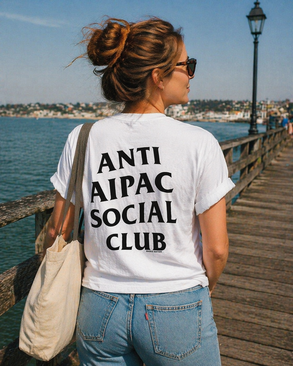 Person wearing a white t-shirt with 'ANTI AIPAC SOCIAL CLUB' text on a wooden pier.